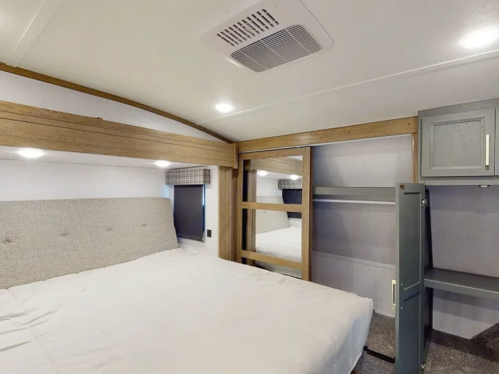 RV rental bedroom interior featuring a spacious bed, built-in storage, and a mirrored sliding closet door.. Keystone RV Eddie Bauer Signature 360LF 2024