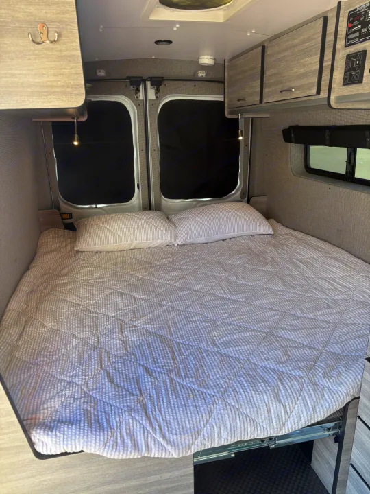 Cozy RV rental bed with built-in storage and blackout window covers, ready for your next adventure.. Ford Transit 2017