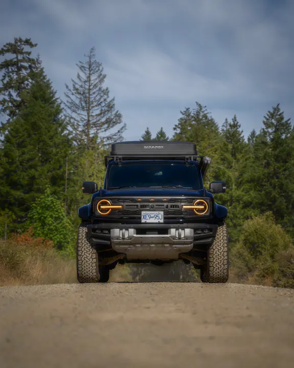 A black Ford Bronco SUV with a rooftop tent, ideal for an RV rental and off-road adventures, on a gravel road in the forest.. Ford Van 2024