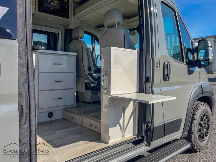 Inside a stylish camper van: light wood cabinets, microwave, and fold-down table, perfect for an RV rental.. Thor Tellaro 2026