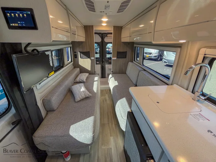 RV rental's inviting interior with dual sofas, wall-mounted TV, kitchen counter with sink, and overhead storage.. Thor Tellaro 2026