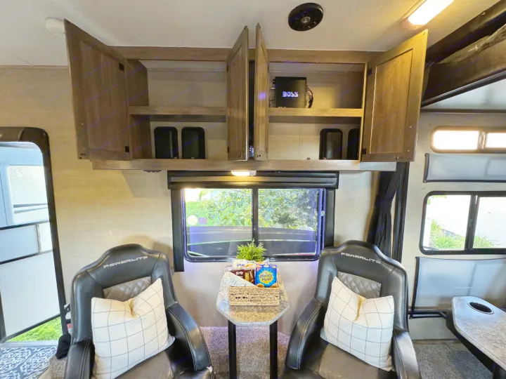 RV rental interior: Two comfy Powerlite chairs, a snack table, scenic windows, and open overhead cabinets for storage.. Pacific Coachworks Powerlite 2017