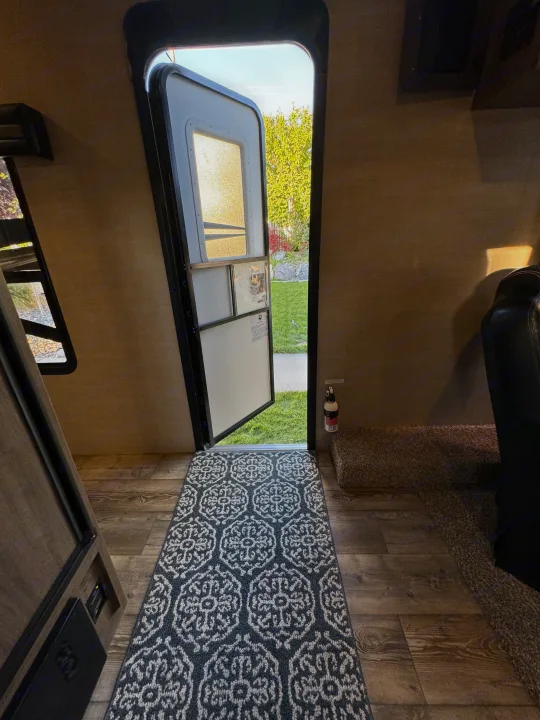 RV rental interior with open door, showing wood floor, runner rug, and outdoor view. Fire extinguisher mounted.. Pacific Coachworks Powerlite 2017