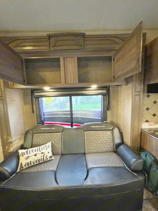 Inside an RV rental: A dark, diamond-patterned sofa, open wood cabinets, and large windows revealing outdoor scenery.. Pacific Coachworks Powerlite 2017
