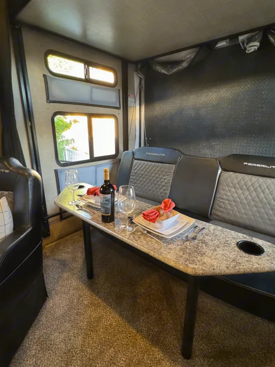 Cozy RV rental interior: dining table with wine, place settings for two & comfy bench seats. Perfect for travel!. Pacific Coachworks Powerlite 2017