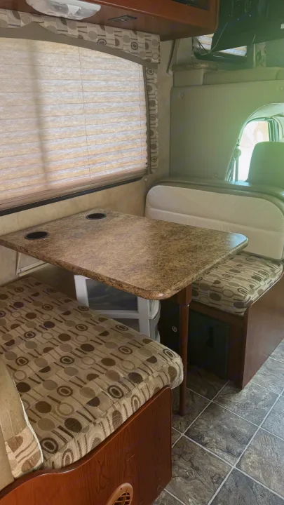 RV rental dinette setup featuring a table with cup holders, patterned bench seats, and privacy blinds.. Thor Chateau 2012