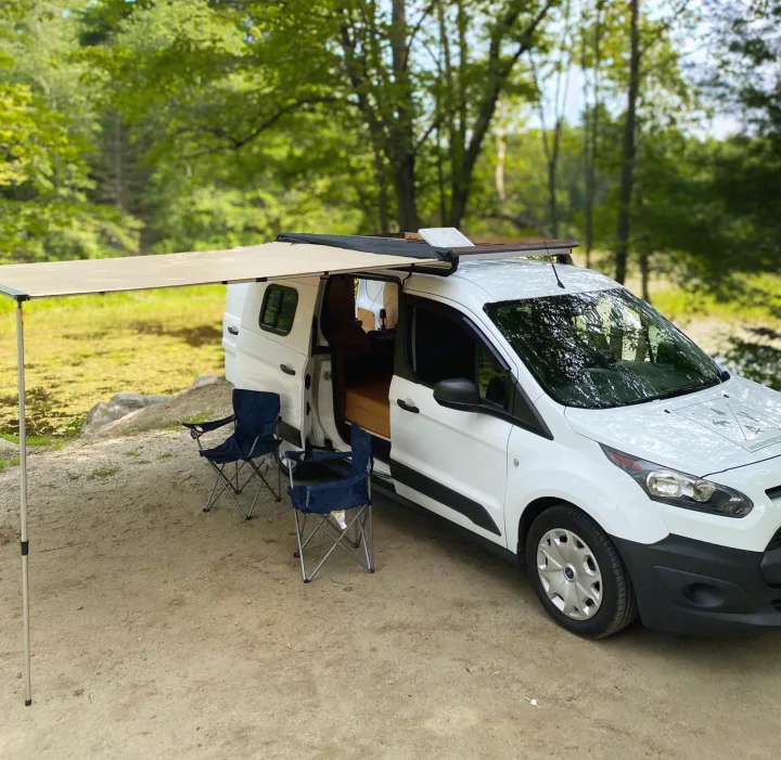 White camper van RV rental with an awning and chairs, perfect for peaceful camping by the forest and pond.. Ford Transit Custom 2015