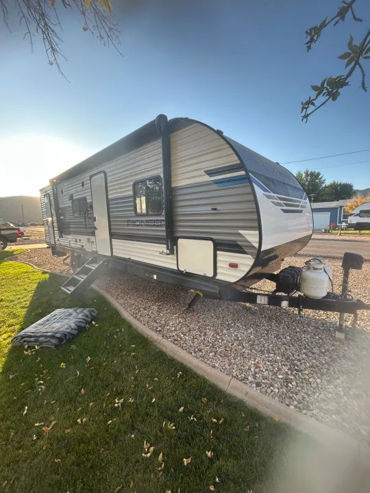 A modern travel trailer, perfect for an RV rental adventure, parked on gravel with an awning extended.. Heartland RVs Pioneer 2022