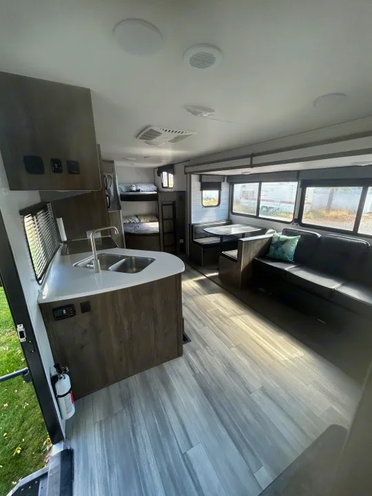 Modern RV rental interior featuring a full kitchen, dining booth, comfy sofa, and cozy bunk beds.. Heartland RVs Pioneer 2022