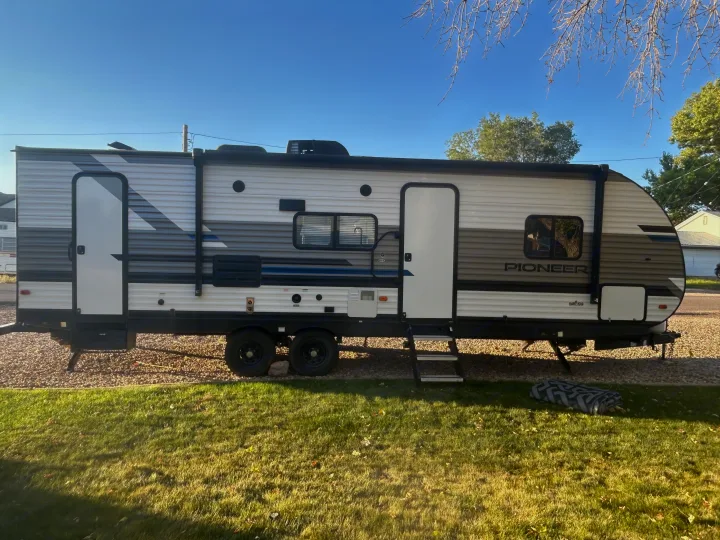 This image shows an RV rental, a white and gray travel trailer parked on gravel, ideal for outdoor adventures.. Heartland RVs Pioneer 2022