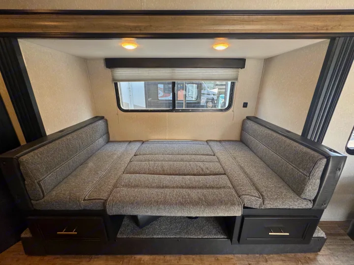 RV rental dinette with grey cushions converts to a bed, showing built-in storage drawers.. Forest River Cherokee Wolf Pup 2021