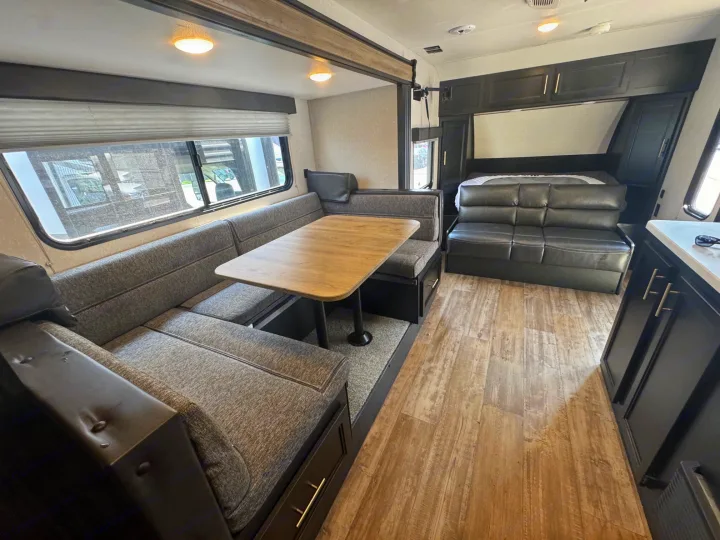 Modern RV rental interior: U-shaped dinette, sofa, and bed with wood-look floor. Cozy travel camper living space.. Forest River Cherokee Wolf Pup 2021