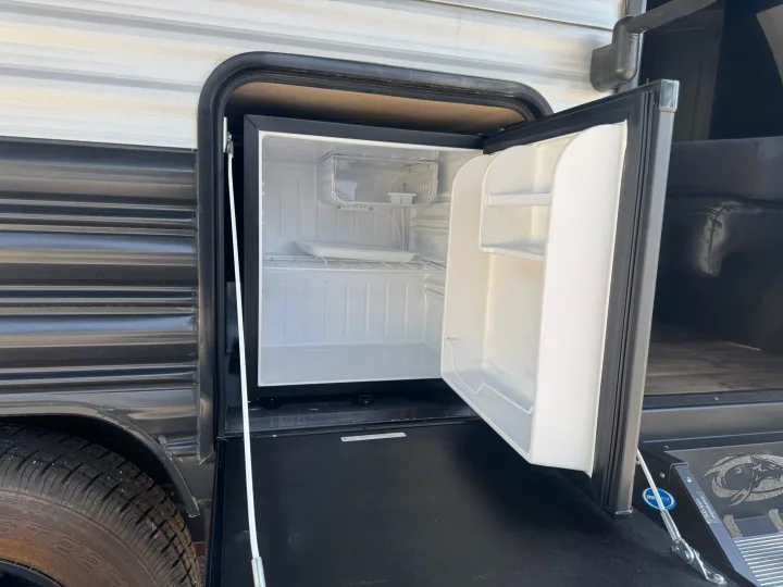 An open mini-fridge in an RV rental's outdoor kitchen area, ready for cold drinks and snacks during your camping adventure.. Forest River Cherokee Wolf Pup 2021