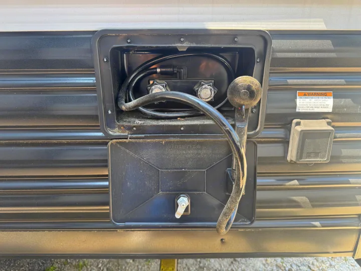 An RV rental's side panel displays an open outdoor shower, closed winterize access, and electrical warning, detailing utility hookups.. Forest River Cherokee Wolf Pup 2021