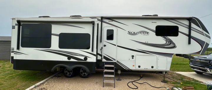 Large white Solitude fifth-wheel RV rental with black accents, parked on gravel, ready for adventure.. Grand Design Solitude 2022