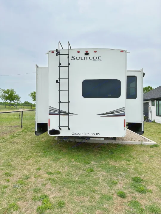 Grand Design Solitude Fifth Wheel RV rental. Rear view showing ladder & extended slide-outs, parked on grass.. Grand Design Solitude 2022