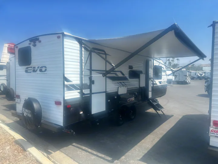 White Forest River EVO travel trailer with an extended awning and outdoor grill, ready for RV rental.. Forest River Evo 2400bhl 2024