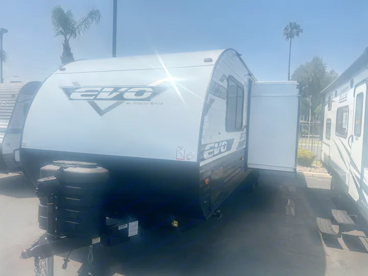 New white EVO travel trailer for rv rental on a sunny day. See its front hitch, windows, and extended slide-out.. Forest River Evo 2400bhl 2024