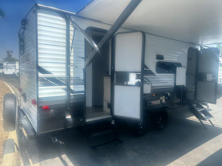 A modern, white and grey RV rental with its awning extended, open doors, and an outdoor cooking station visible.. Forest River Evo 2400bhl 2024