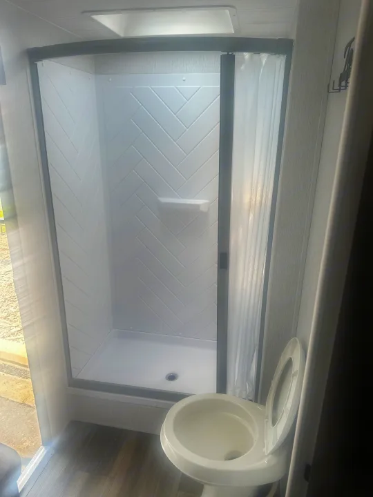 Inside an RV rental: a bright, clean bathroom with a stand-up shower featuring stylish herringbone walls & a toilet.. Forest River Evo 2400bhl 2024