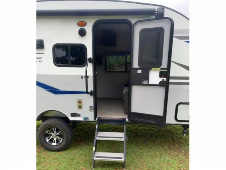 Side view of a white and grey RV rental travel trailer with its door open, showing steps and the interior.. Sonic Lite 2021