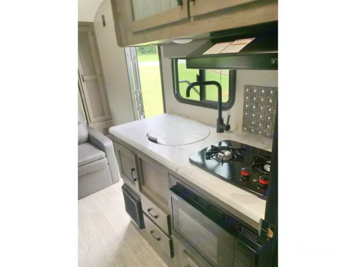Experience an RV rental with this compact kitchen: black stove, oven, sink, and gray seating on light wood-look floor.. Sonic Lite 2021