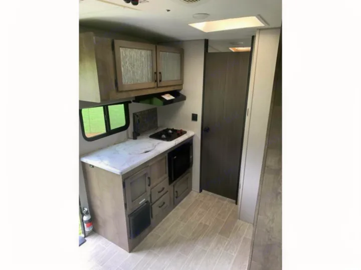 RV rental interior: A compact, modern kitchen with white counters, sink, stove, microwave, and wood cabinets.. Sonic Lite 2021