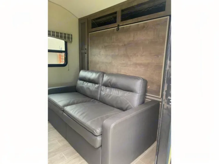 RV rental interior with a grey sofa and wall-mounted murphy bed, optimizing space for comfort and versatility.. Sonic Lite 2021