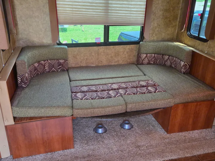 RV rental interior shows a cozy U-shaped dinette with green/brown cushions, convertible to a bed, beside a window.. Coachmen Freedom express ltz 2014