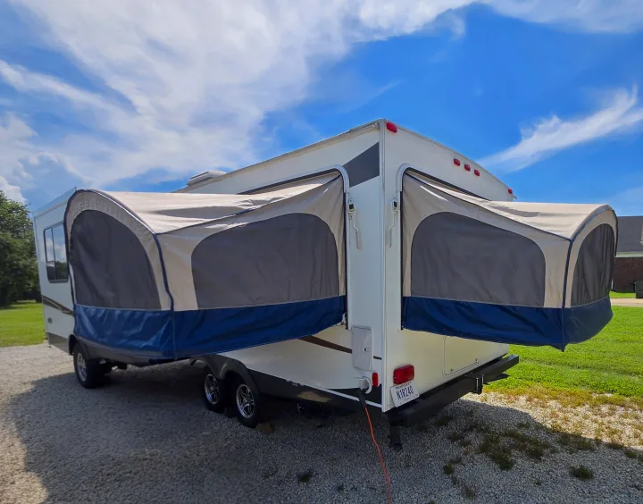 RV rental: Parked white hybrid camper with tan/blue pop-out bunks on gravel driveway. Kentucky plate visible.. Coachmen Freedom express ltz 2014