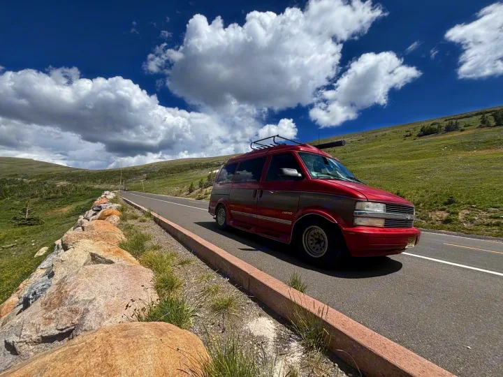 Red van with a roof rack, like an RV rental, parked on a mountain road with green hills & blue sky. Great for trips!. Chevrolet Astro Van 2000