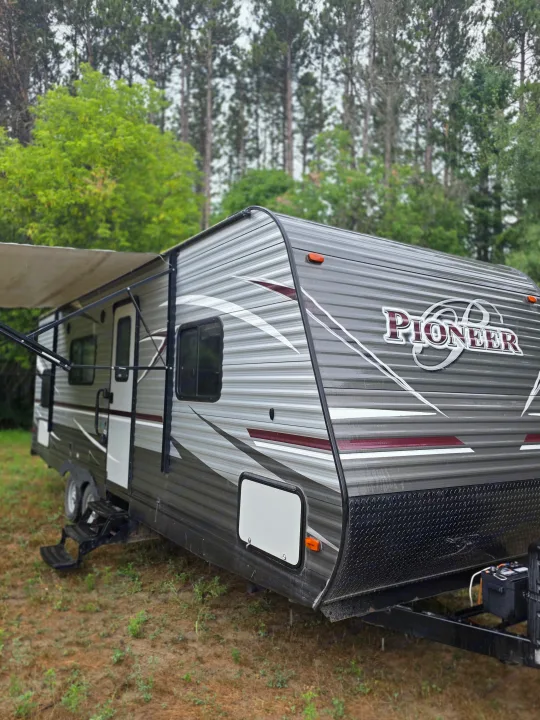 Explore the outdoors! This grey Pioneer travel trailer, ready for an rv rental, is parked in a scenic wooded area.. Heartland RVs Pioneer 2017