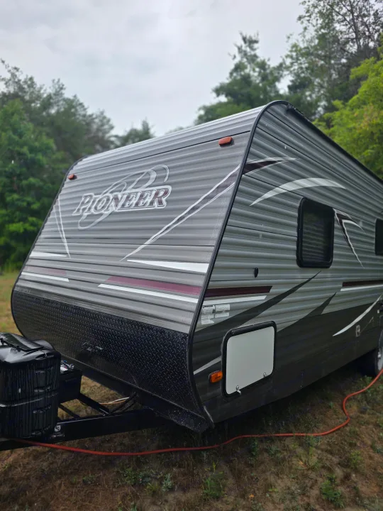 A gray Pioneer RV rental is parked in an outdoor setting with trees under an overcast sky, ready for camping.. Heartland RVs Pioneer 2017
