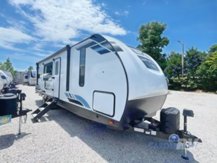 Explore this modern white travel trailer, a recreational vehicle (RV) rental, parked outdoors with steps down and an awning.. Forest River Vibe 2023