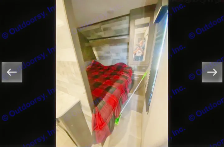 Explore this cozy RV rental's bedroom, featuring a red plaid bed, built-in shelves, and a mirrored closet door.. Coachmen Lantern 2021