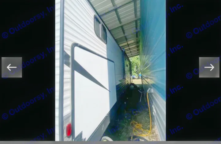Side of an RV rental under a shelter, with its extended slide-out section visible and a yellow power cord on the ground.. Coachmen Lantern 2021