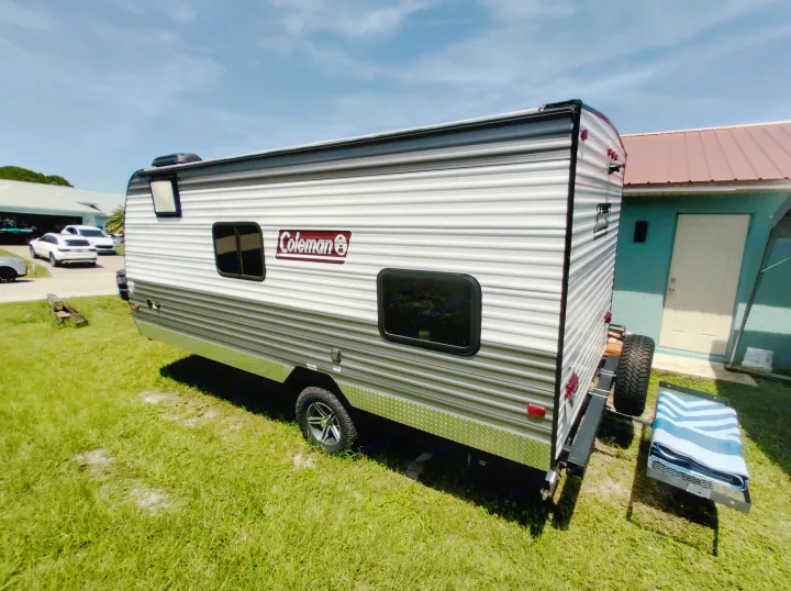 This Coleman RV rental is parked on grass, featuring windows and a rear-mounted spare tire.. Dutchmen 17B 2024