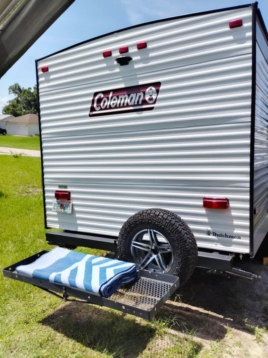Rear view of a Coleman travel trailer RV rental with a cargo carrier, spare tire, and Florida license plate.. Dutchmen 17B 2024
