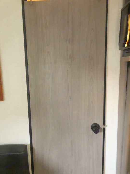 A light gray, wood-grain patterned interior door with a black knob, typical for an RV rental.. Coleman Lantern 17R 2024