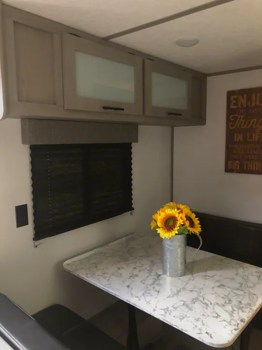 Cozy RV rental interior featuring a dinette with sunflowers, overhead cabinets, and a window with blinds.. Coleman Lantern 17R 2024