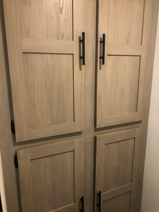 Close-up of light wood-grain cabinets with modern black handles, common storage in an RV rental interior.. Coleman Lantern 17R 2024