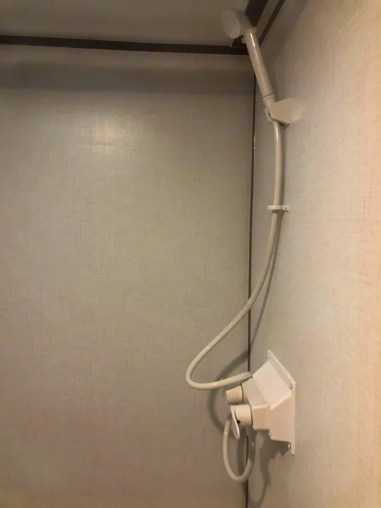 A simple handheld shower unit in an RV rental's compact bathroom, showing the showerhead, hose, and controls.. Coleman Lantern 17R 2024