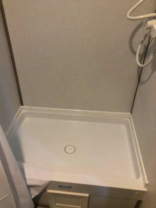 Compact shower stall in an RV rental, featuring a white pan, textured walls, and a central drain.. Coleman Lantern 17R 2024