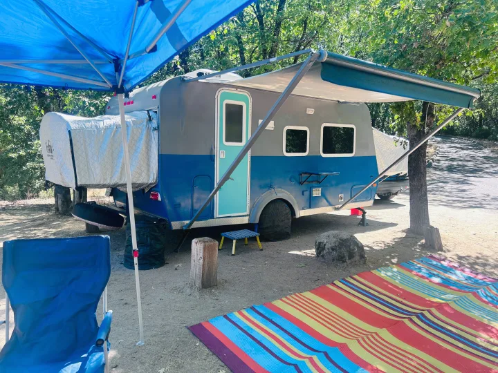 RV rental site: a blue & grey camper with awning, a bright blue canopy, and a striped ground mat.. Forest River M-17 2005