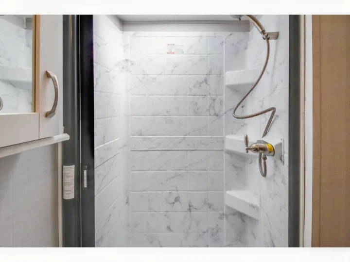 Clean, compact shower with marble-patterned walls and a handheld showerhead, ideal for an RV rental.. Gulf Stream Conquest 2023