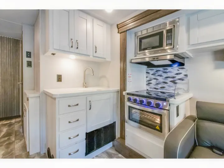 Explore this RV rental's bright kitchen: white cabinets, sink, microwave, stove, and oven. Ready for your travel needs.. Gulf Stream Conquest 2023