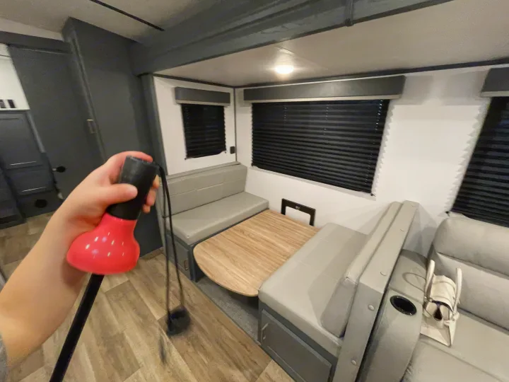 Modern RV rental interior with grey dinette, wooden table, and dark blinds. A hand holds pink exercise equipment.. Keystone RV Bullet Ultra Lite 2022