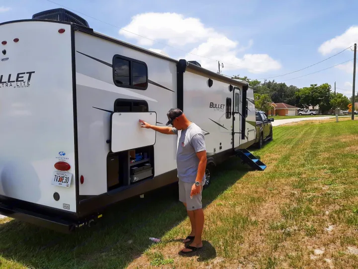 Man preps his rv rental, a Bullet Ultra Lite travel trailer, by opening its outdoor kitchen for a fun camping trip.. Keystone RV Bullet Ultra Lite 2022
