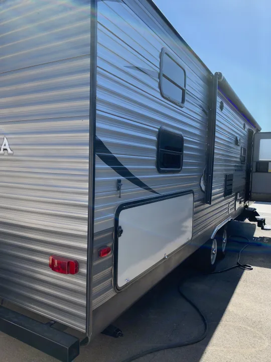 Side view of an rv rental, detailing its corrugated siding, windows, storage hatch, and a deployed awning with blue lights.. Coachmen Other 2018
