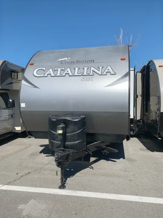 Front view of a grey Coachmen Catalina SBX travel trailer, a spacious RV rental, parked on asphalt under a clear blue sky.. Coachmen Other 2018